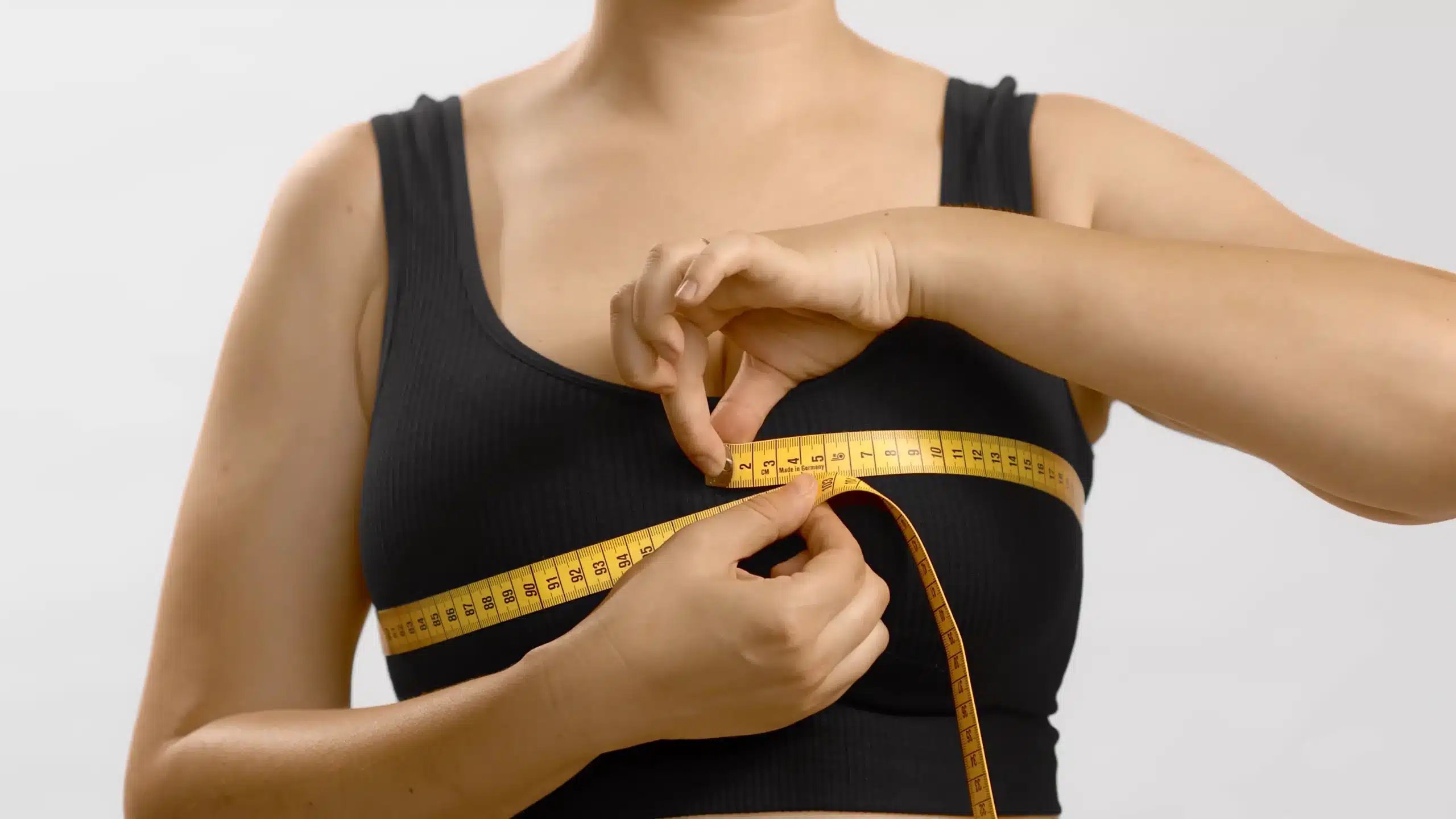 Breast Augmentation In Tijuana, Mexico 17 Woman measuring her bust with a tape measure to determine current cup size and desired results before breast augmentation surgery in Tijuana.