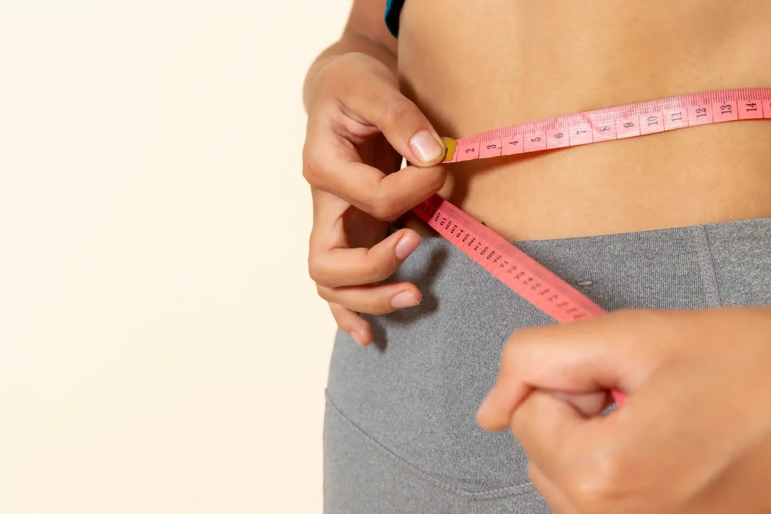 Gastric Bypass in Tijuana, Mexico 19 Woman in fitness wear measuring her waist, maintaining results after bariatric surgery in Tijuana.
