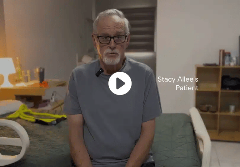 Older man wearing glasses, sitting on a hospital bed, looking at the camera to give his patient testimonial.