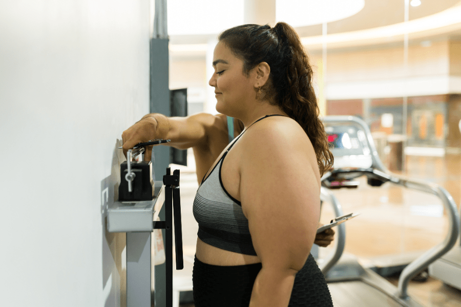 Young woman in athletic wear checking her weight on a scale at the gym, representing progress and support in a bariatric weight loss journey.