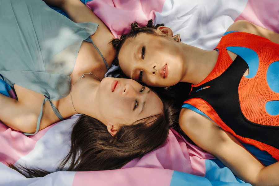 Two people lying on a transgender pride flag, representing gender-affirming surgery options in Tijuana, Mexico.