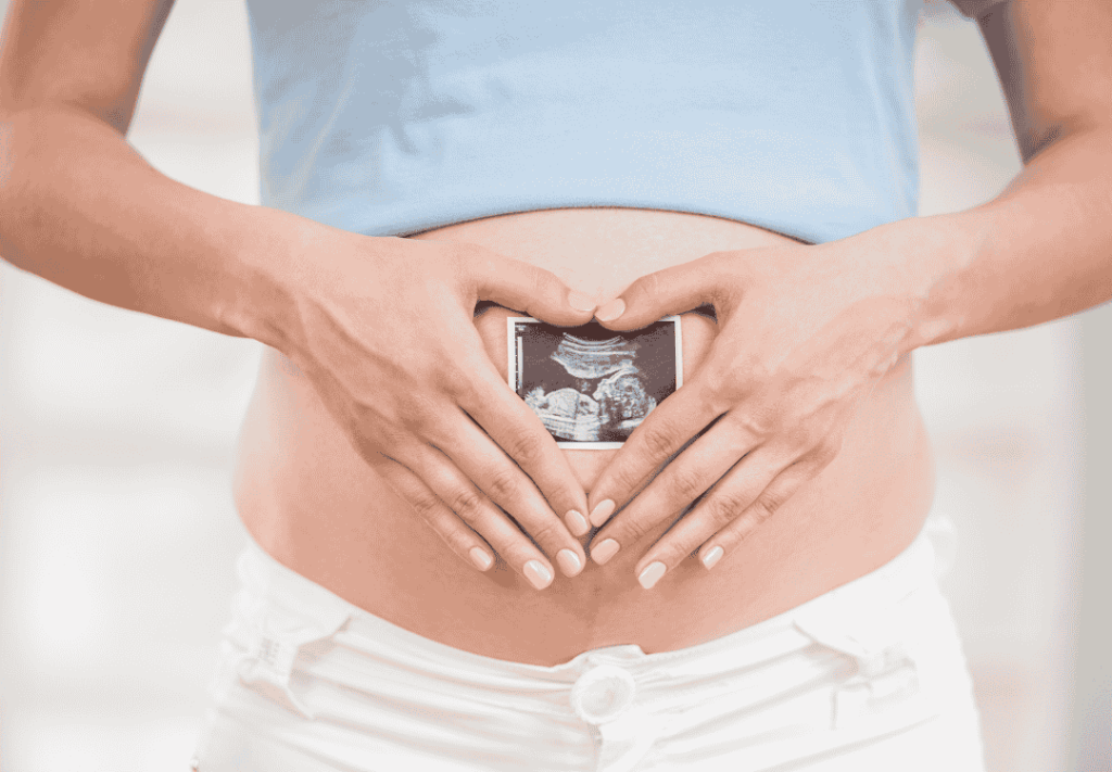 A pregnant woman holding an ultrasound image over her belly, forming a heart shape with her hands, symbolizing the journey to parenthood through fertility treatments.
