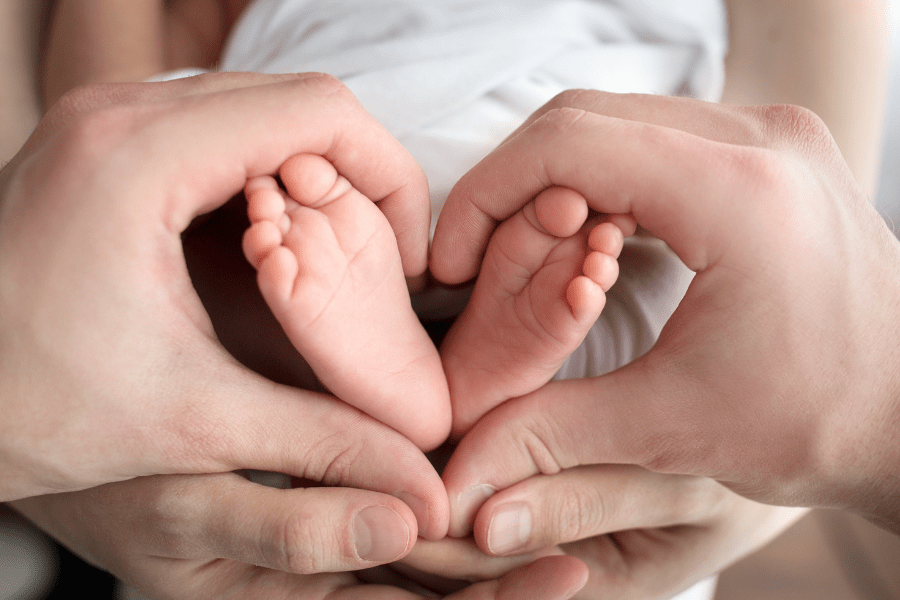Parent’s hands forming a heart shape around newborn baby feet, symbolizing love and care.