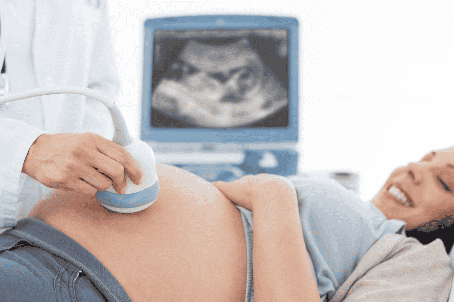 Pregnant woman receiving an ultrasound scan with a doctor, showing baby on the monitor.