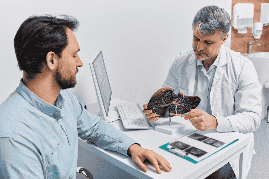A doctor explains gallbladder removal surgery to a patient using an anatomical liver and gallbladder model.