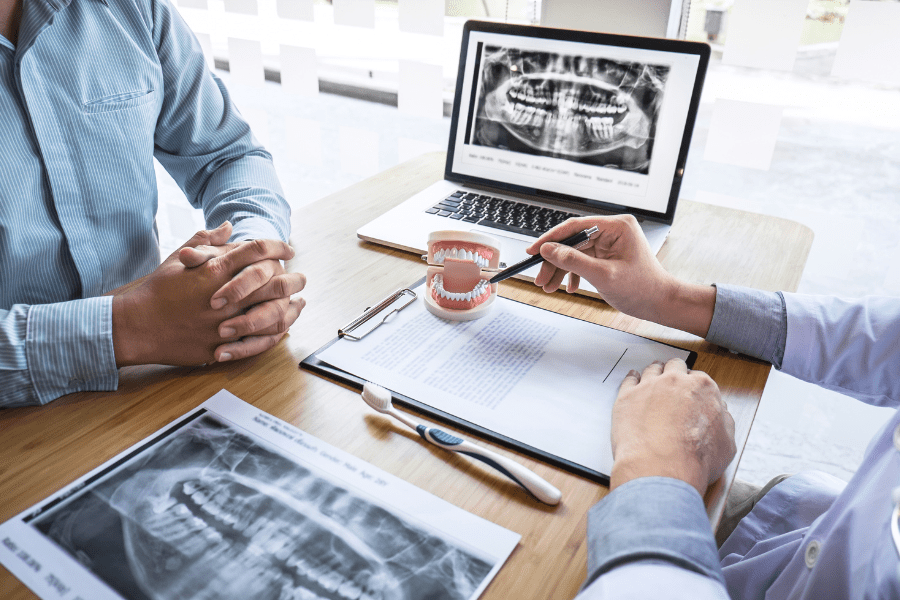 A dental specialist in Tijuana, Mexico, explaining a full mouth restoration procedure to a patient using a dental model and X-ray images. The consultation covers dental implants, veneers, crowns, and bridges as part of a cost-effective dental tourism solution.
