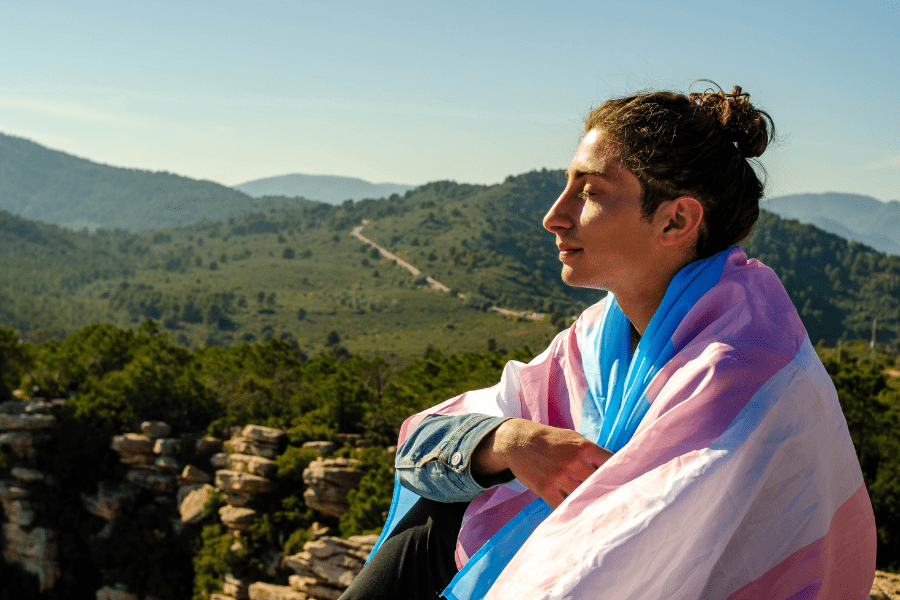 A person wrapped in a transgender pride flag, symbolizing confidence and freedom after FTM top surgery with HWBazaar.