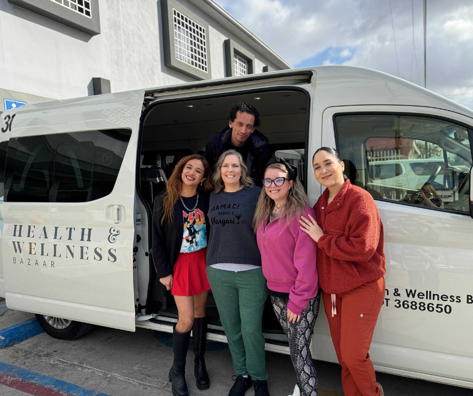A group photo of a patient and several smiling Health & Wellness Bazaar team members next to a branded transport van in Tijuana.