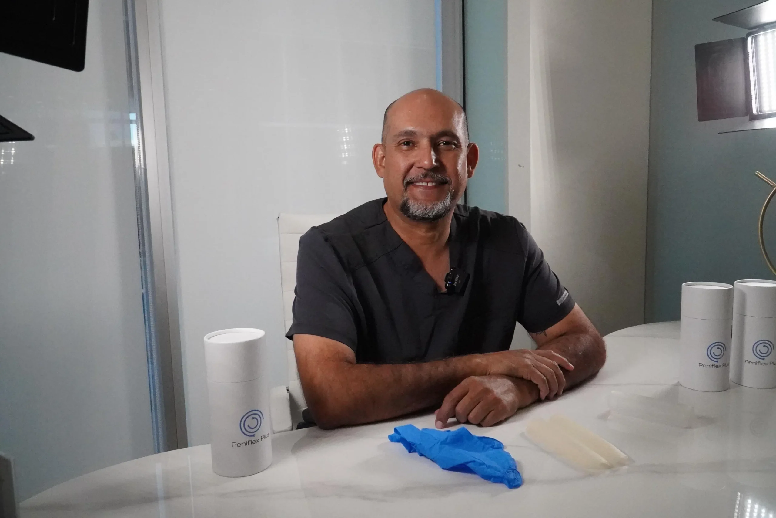 Vetted Doctors in Tijuana | Health & Wellness Bazaar 21 Professional portrait of Dr. Ivan Aguilar, urologist. The doctor, with over 20 years of experience, smiles at the camera in his office and is wearing gray surgical scrubs.