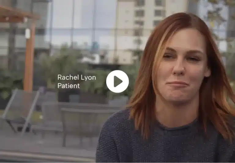 Rachel Lyon, a patient, in a modern outdoor setting, with an emotional expression as she gives her testimonial.