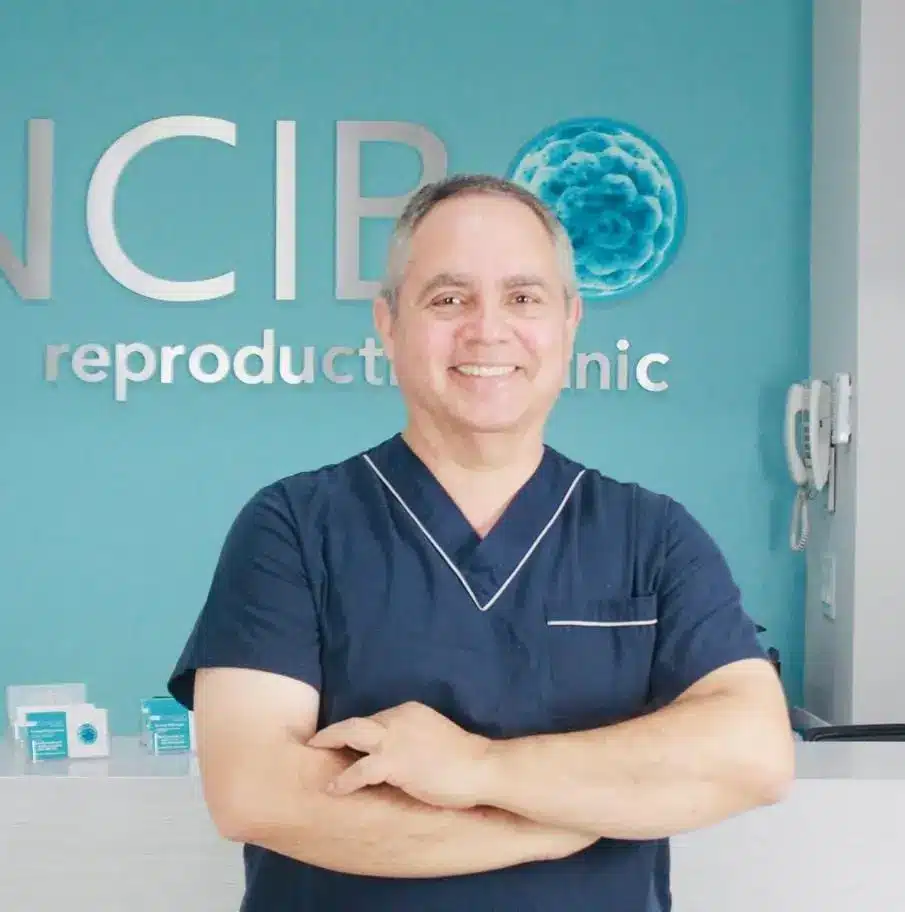 IVF in Tijuana, Mexico 16 Portrait of a smiling IVF specialist in Tijuana standing in front of the CIB Reproductive Clinic logo, welcoming international patients for fertility treatments.